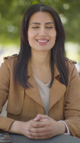 Vertical-Video-Portrait-Of-Smiling-Muslim-Woman-Sitting-At-Outdoor-Table-On-City-Street